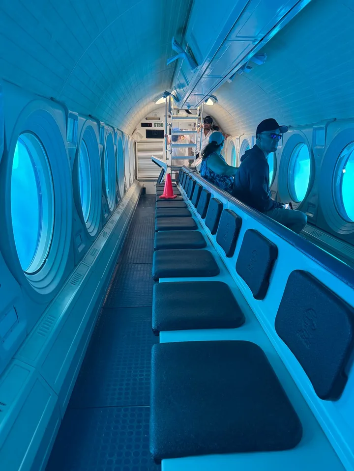 Passengers seated along the row of round viewports inside the submarine
